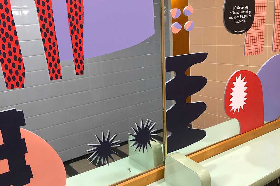 Viva con Agua Toilette: Buntes Design mit Formen und Mustern an Wand und Spiegel. Kunst im Badezimmer.