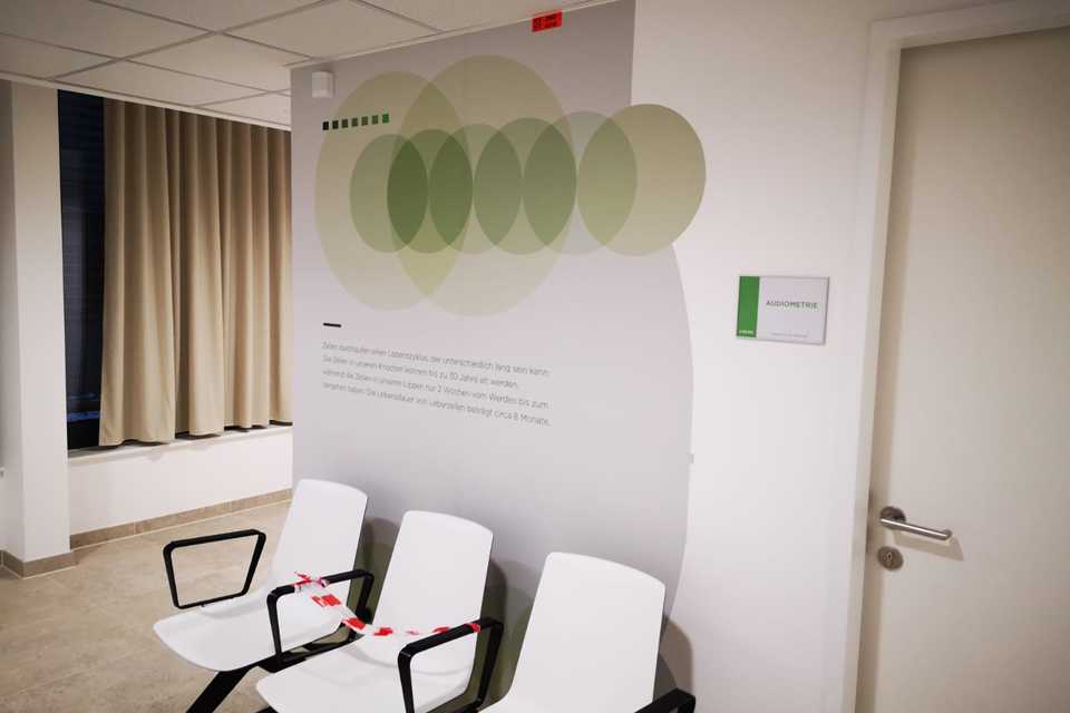 SVS Interiors: Wartebereich mit Wandbeklebung, Stühlen und Audiometrie-Hinweis. Modernes Design.