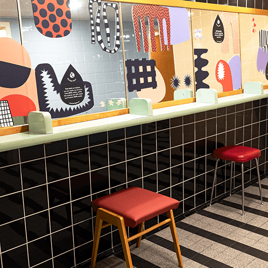 VIVA CON AGUA Toilette mit bunten Grafiken und roten Hockern.