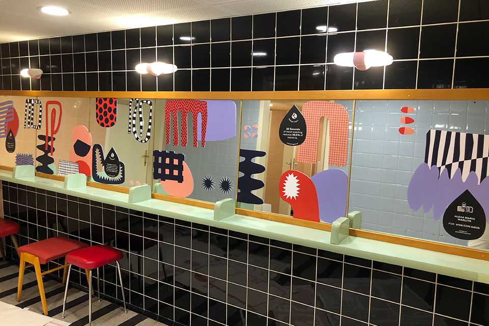 VIVA CON AGUA Toilette mit Kunst. Buntes Design mit schwarzen Fliesen. Saubere Sanitäranlagen.